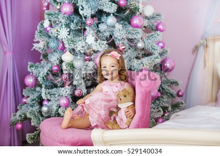 Happy cheerful little girl excited at Christmas Eve, sitting under decorated illuminated Tree. Greeting card or cover, horizontal with copy space.