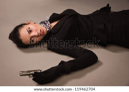 Detective scene imitation. Woman in a black suit with gun lying on the floor