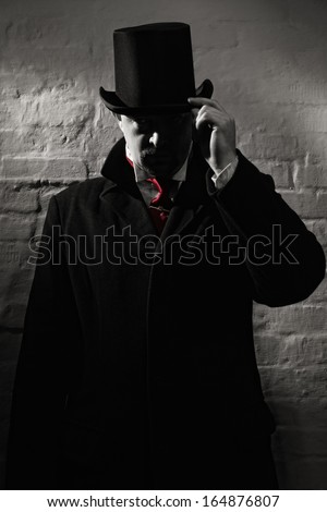 Man in the black coat, top hat and in a red tie on a wall background
