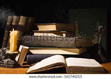 Vintage still life. Old books and candles on wooden table on dark background