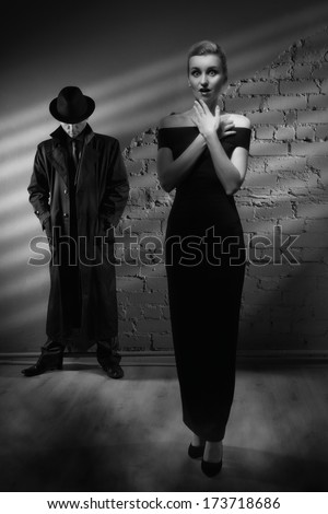 Film noir. Woman in a long black dress and a man in a raincoat and hat