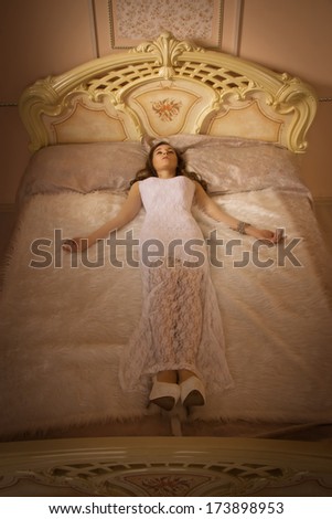 Elegant girl in evening dress lying on the bed in an elegant bedroom