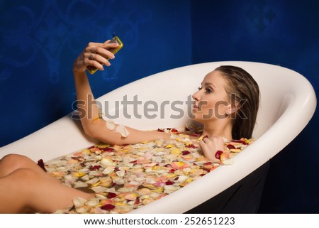 Beautiful sexy woman in bath with flowers petals while using the smart phone. she is doing a selfie