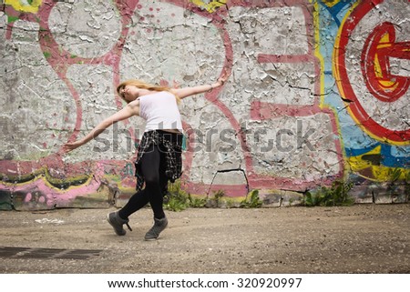 Young girl dancing on graffiti background. Dancing and urban culture concept. Film grain effect