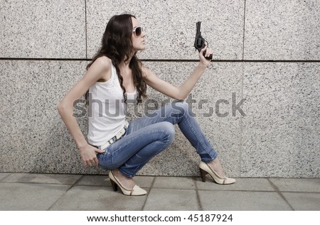 Beautiful stylish girl with a revolver on a wall background