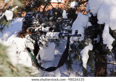 Sniper girl in white camouflage aiming with rifle at winter forest.