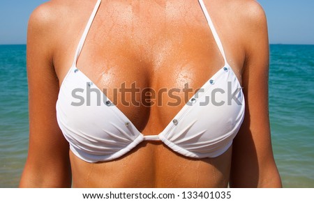 Beautiful large tan female breast in a white bathing suit against the sea
