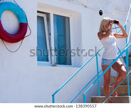A beautiful young blond woman lifeguard watching through binoculars at the rescue station.