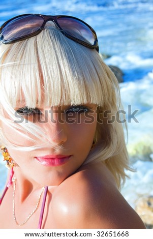 Portrait of young beautiful tanned blond sexy woman with bright blue eyes against the dark blue sea