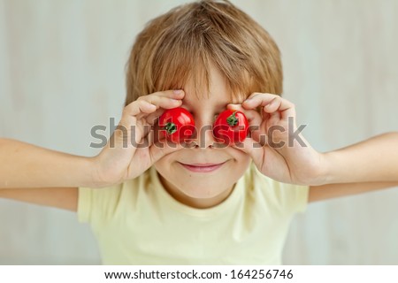 Portrait of happy boy holding ripe tomatoes before his eyes