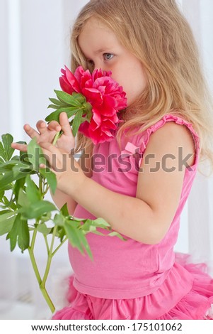 Beautiful little girl posing with a large bouquet of flowers in a luxurious pink dress at home.