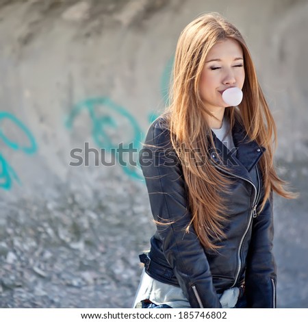 Fashionable beautiful woman posing on wall background. Blow bubble gum. Outdoor lifestyle.