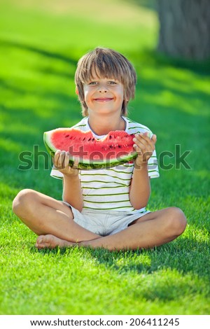 Funny kid eating watermelon outdoors in summer park. Child, baby, healthy food