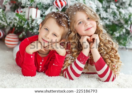 Happy brother and sister are playing on the floor near Christmas tree.