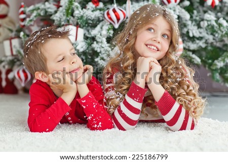 Happy brother and sister are playing on the floor near Christmas tree. little friends enjoying New Year party, Christmastime holidays, best friends, happiness concept