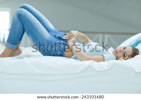 Woman dressed. Young blond hair woman lying on the bed and pulling on skinny jeans