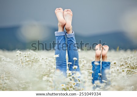 Healthy feet of family with daisy flowers on green grass against blurred spring background. Farmland vacations concept