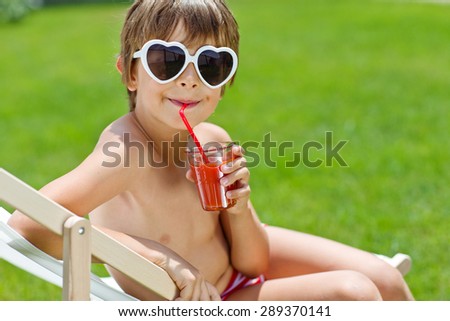 Little boy drinking juice on a lounger. A boy holding a glass of juice, big blue eyes looking at the camera