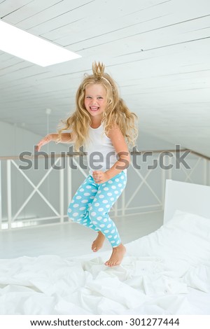 A happy young girl in white dress having fun jumping on bed