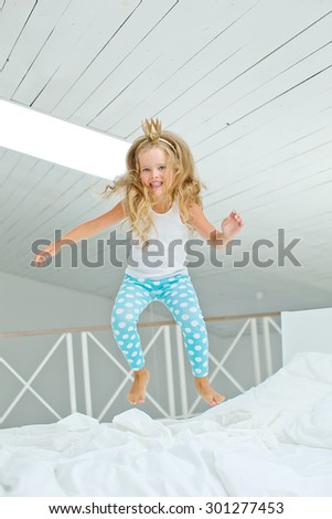 A happy young girl in white dress having fun jumping on bed