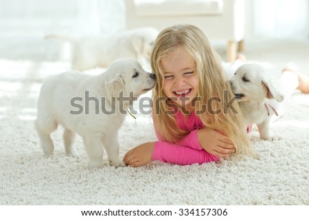 Little girl lying on the mat with labrador, smiling at camera at home in the living room