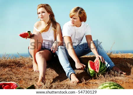 Young couple sitting in the garden and eat watermelon