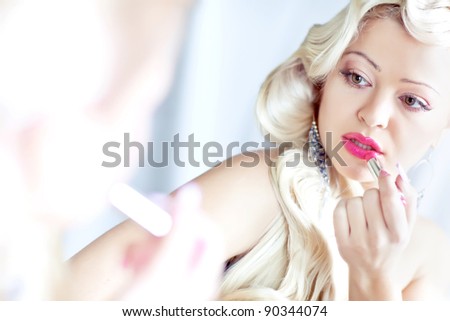 Young woman applying lipstick looking at mirror