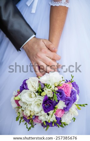 bride holding a wedding bouquet, groom gently embraces her hands