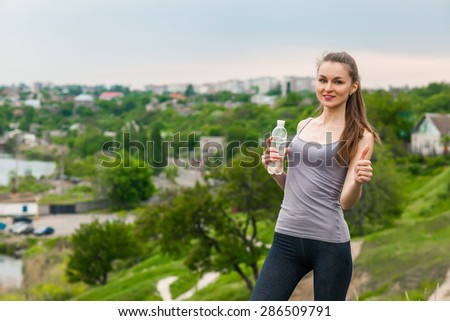 Athlete woman refreshing with Bottle of water after running workout outdoors. Woman giving a Thumbs up, Healthy active Lifestyle