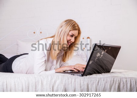 A smiling woman lying down the bed in front of her laptop with her legs raised slightly