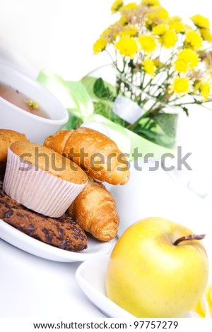continental breakfast with croissants, cake, chocolate cookies, apple and tea