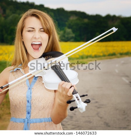 Young beautiful violin player by country road