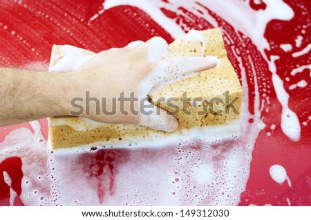 Human arm with sponge soap washing red car surface
