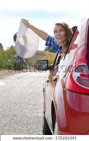 Young happy woman holds sun hat looking from car window
