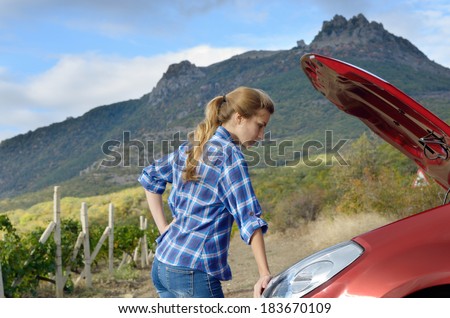 Young woman near broken car needs assistance looking under opened hood