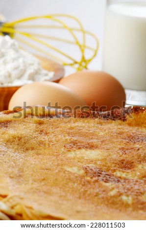 Milk, flour, whisk, pancakes and eggs on wooden table