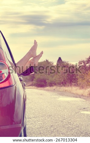 Female bare feet stick out of car window on mountain background. Travel concept.