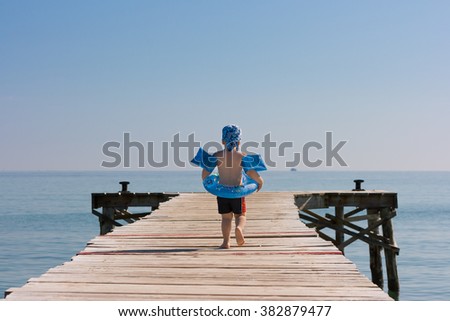 3 years old boy walking on beach wooden pier ready to swim in a sea. Summer outdoor activities with children on the beach. Blue sky and ocean in the morning. Safety first.