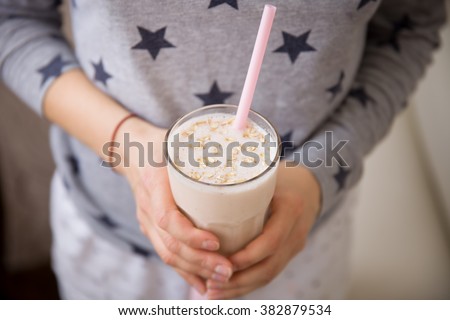 Young woman with a big glass of healthy smoothie served with a straw and oats. Hands holding milkshake. Stars background. Dairy snack or breakfast. Horizontal view.