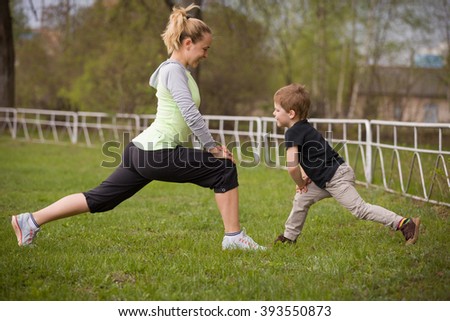 Happy son and mother are doing exercises in the summer park. on the stadium, outdoor. Sport activities with children. Healthy lifestyle. Fitness exercises. Young mother and son are stretching together