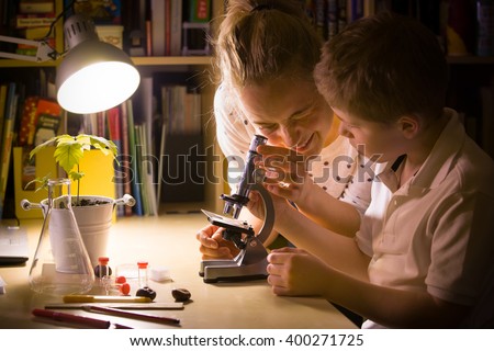 Young mother and elementary school kid boy looking into microscope at home. Family studying samples under the microscope. Science activities with children. Preparing for science lesson.