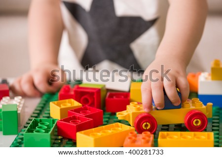 Close up of child\'s hands playing with colorful plastic bricks at the table. Toddler having fun and building out of bright constructor bricks. Early learning.  stripe background. Developing toys