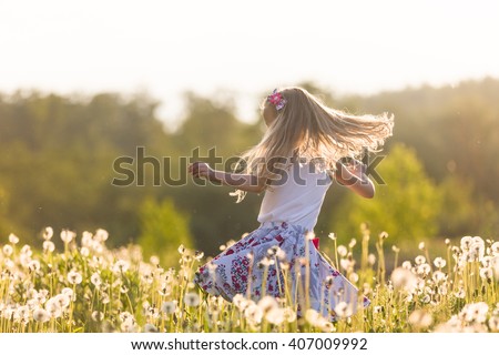Girl running on the field of dandelions on summer sunset. Beautiful little kid girl  dancing on dandelion meadow with summer sunset. Summer fun outdoors.