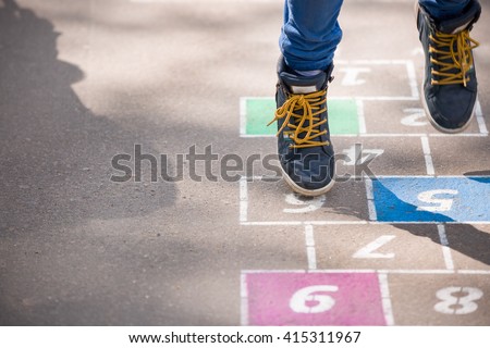 Closeup of boy\'s legs and hopscotch drawn on asphalt. Child playing hopscotch on playground outdoors on a sunny day. outdoor activities for children.