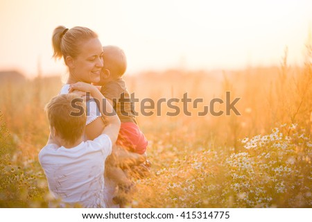 Beautiful young woman with two boys on the daisy meadow on a sunny day. Happy family on summer sunset. Kid boy giving flower to his mother. Mum with baby and kid.