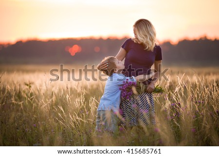 Cute kid boy hugging his mother on a summer meadow on beautiful summer sunset. Happy family together. Mum and child. Motherhood and childhood. Family walking in the field. Outdoors.
