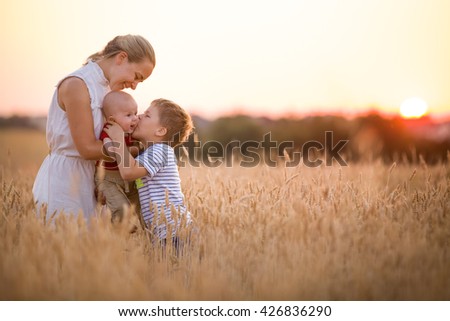 Happy family enjoying sunset in wheat field. Beautiful young woman with adorable baby boy and kid. Mother hugging her two children on a meadow on a sunny evening. Mom and sons. Outdoors.