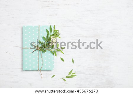 Top view on decorated birthday gift with garden tree branch and flowers. Packing present for the party. Wrapping gift with flower decor and turquoise paper. Holidays concept. Flat lay.