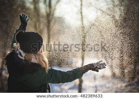 Portrait of young woman throwing the snow, outdoors. Smiling girl walking in a winter park and having fun on a cold sunny day.