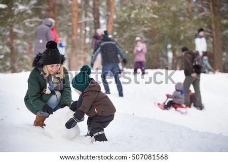 Cute little toddler boy and his mother playing with snow and making snowman. Child having fun outdoors in winter.